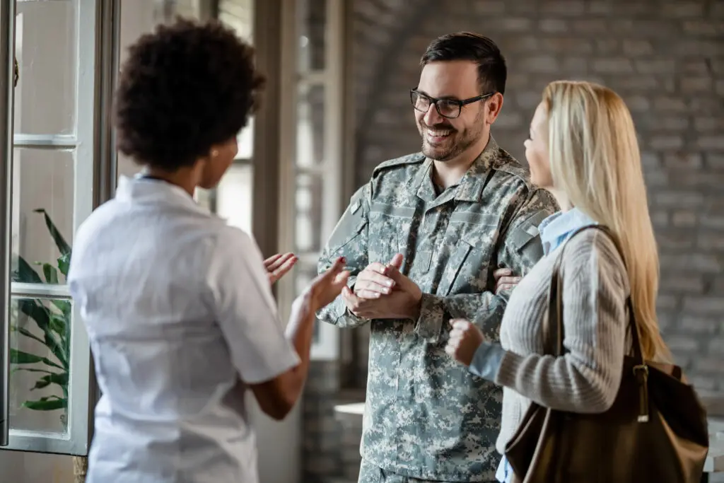 Happy army soldier and his wife communicating with African American healthcare worker while having consultations at the clinic.